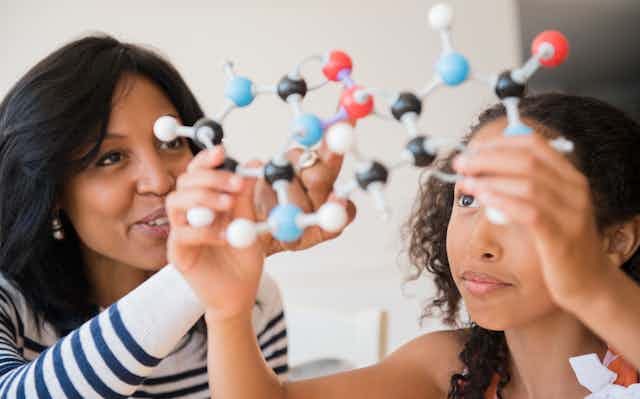 A teacher and a student hold up a model of molecules.
