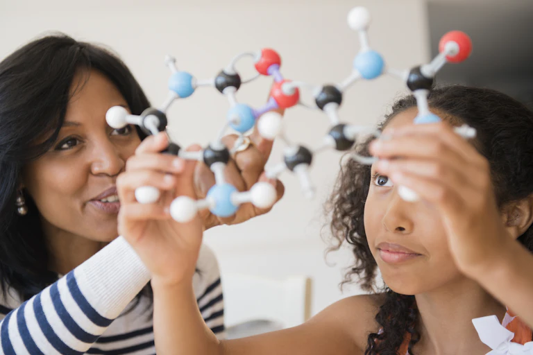 A teacher and a student hold up a model of molecules.