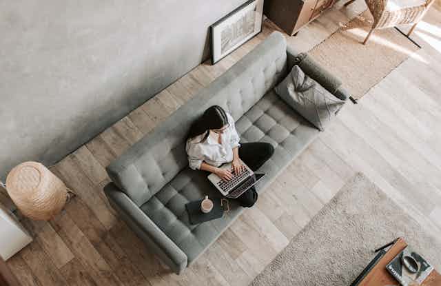 A woman sits on a grey couch with her laptop.