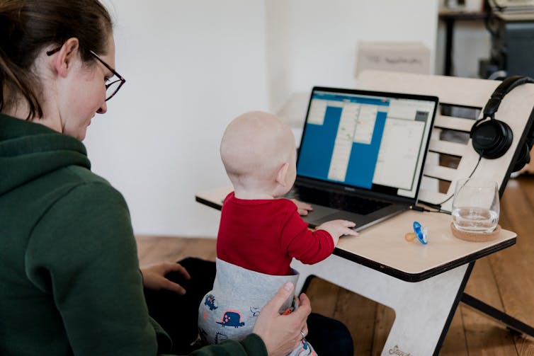 A baby sits on a woman's lap and looks at her laptop.