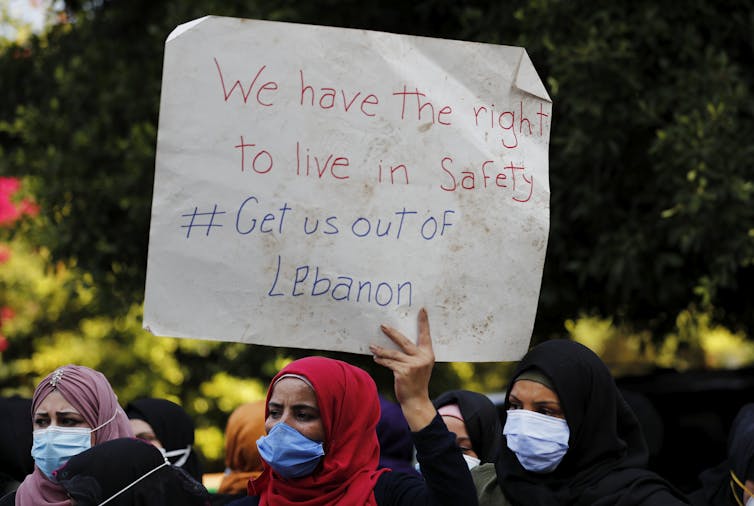 Women hold up a protest sign reading 'We have the right to live in safety. Get us out of Lebanon.'