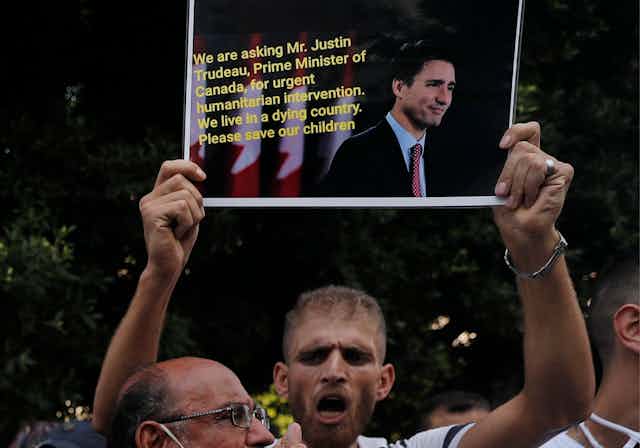 A man holds up a sign pleading for help from Justin Trudeau.