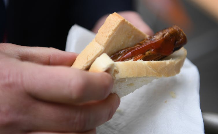 Hand holding a sausage, sauce and bread.
