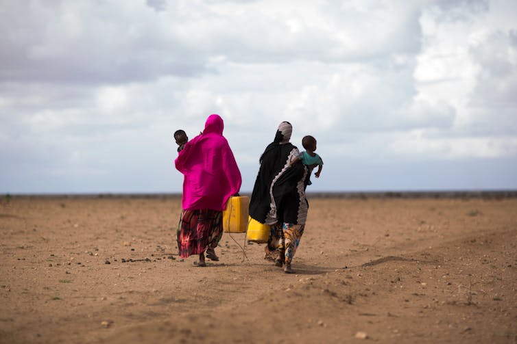 Two women and their babies walk across a dry desert.