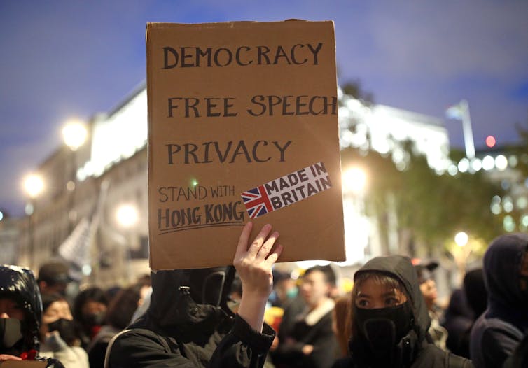 Hong Kong pro-democracy protester in London holds sign promoting democracy, free speech and privacy.