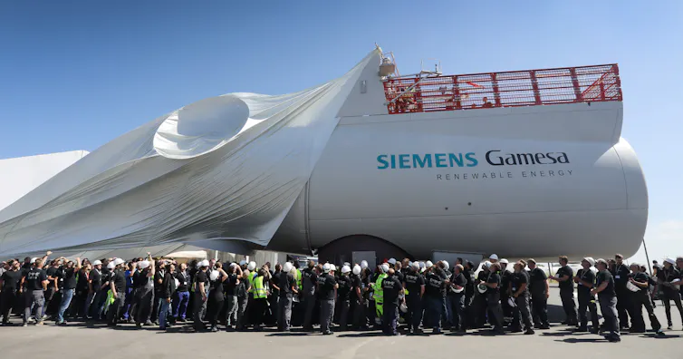 Workers unveil a massive white wind turbine engine.