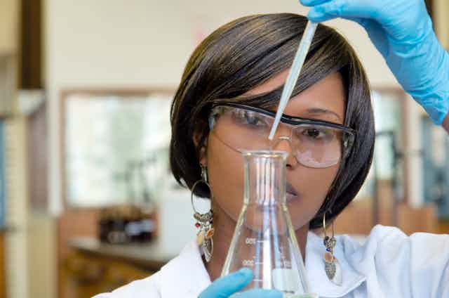 Woman scientist in lab adding drops with pipette to flask