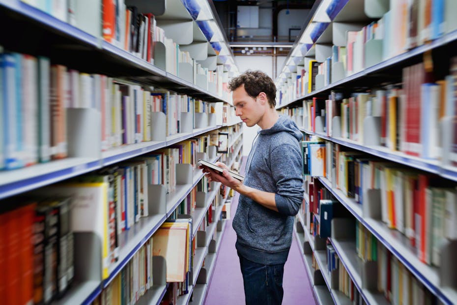 Man standing in between library shelves reading book