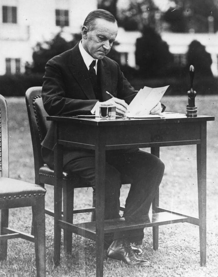 President Calvin Coolidge filling out his absentee ballot at a desk outside of the White House.