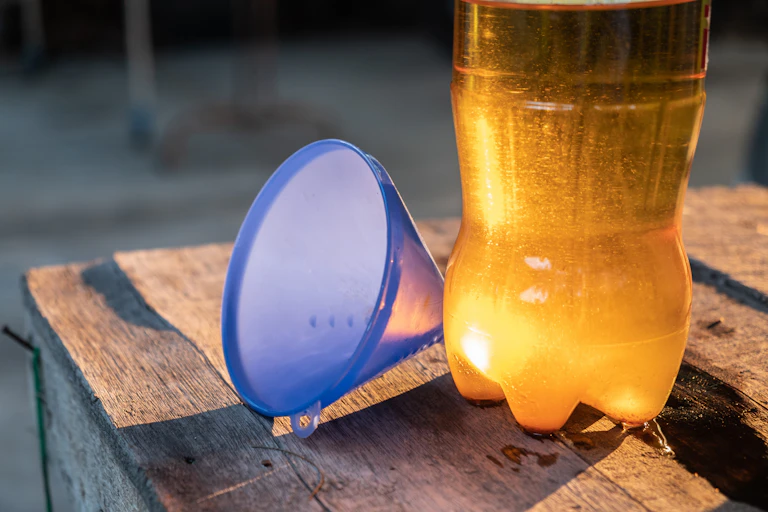 Botella de plástico llena de aceite usado y embudo azul.