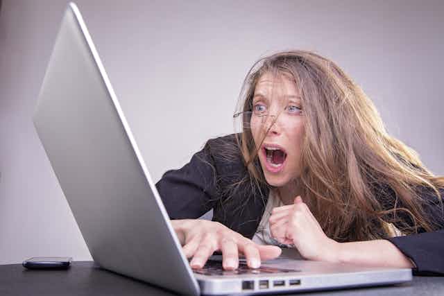 Woman with messed up looks in horror at computer screen.