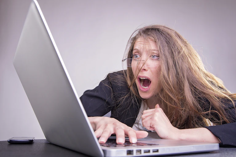 Woman with messed up looks in horror at computer screen.