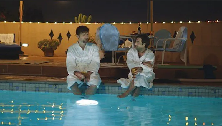 Actors Adam Scott and Jason Schwartzman lounge by the pool in bathrobes in a scene from 'The Overnight.'