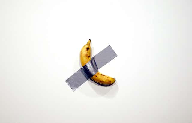 Banana taped to wall with silver duct tape.
