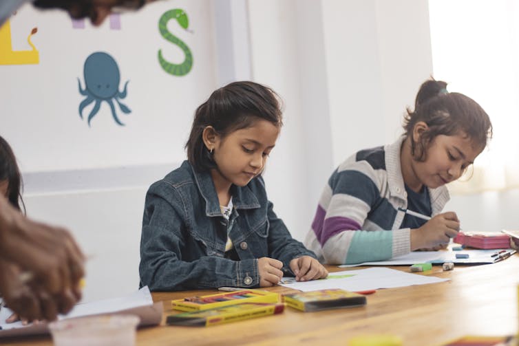 Two girls sitting at a table in a classroom doing school work.