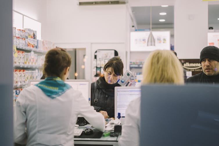 A woman wearing a black jacket looks tired as she pays for her purchase at a pharmacy.