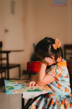 A girl with a bow in her hair sits at a school desk looking at a map.