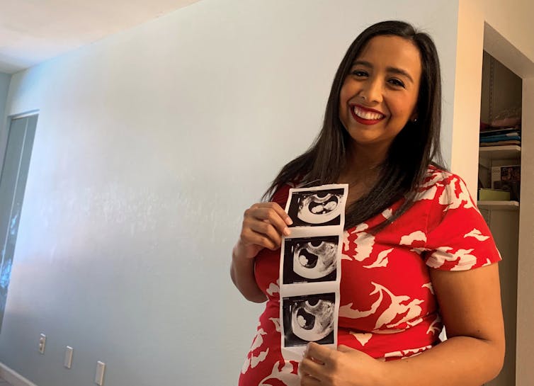 A smiling woman holds up a strip of sonogram images.