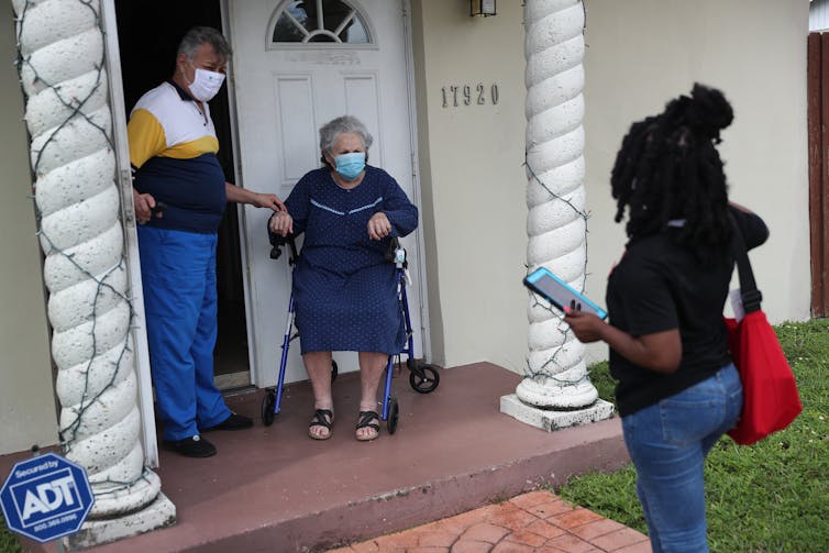 A woman speaks with two people on their doorstep.