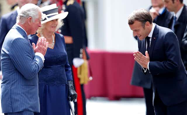 Prince Charles and Emmanuel Macron greet each other with prayer hands