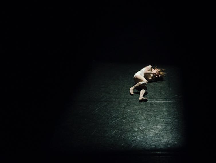 Woman lies in spotlight onstage