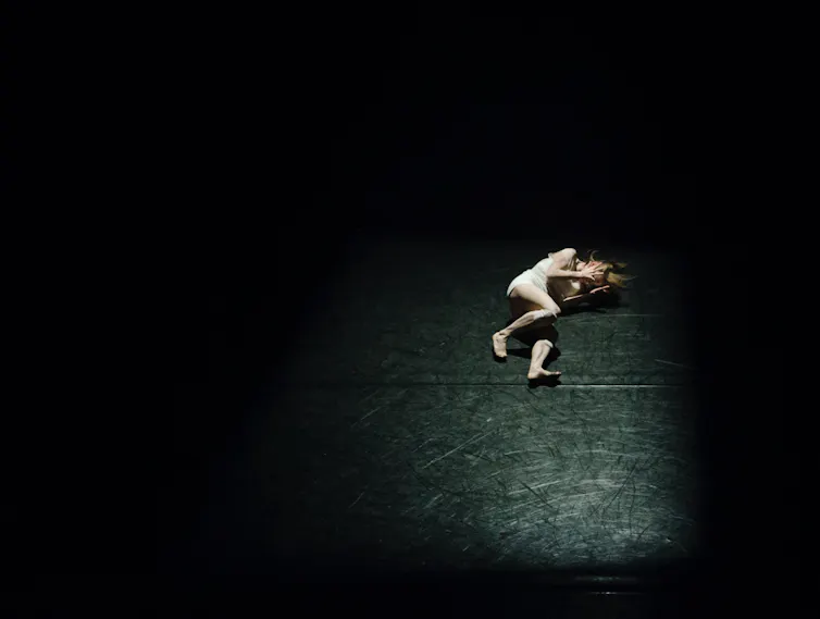 Woman lies in spotlight onstage