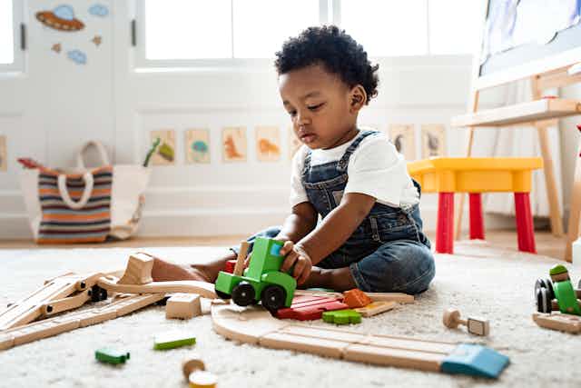 A young boy plays with wooden toys on the floor.