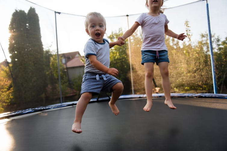 Two young children jumping on a trampoline.