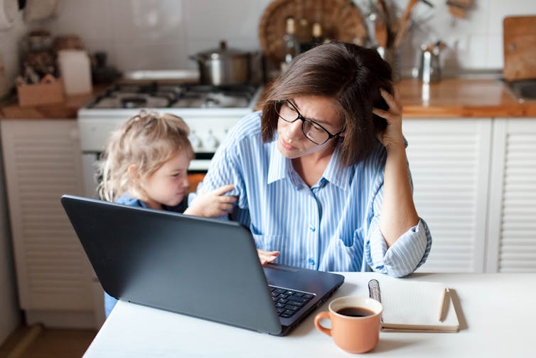 A mother tries to work on her laptop while her young child is bothering her.