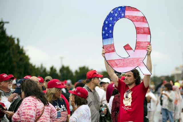 A man holds up a large letter Q at a protest.