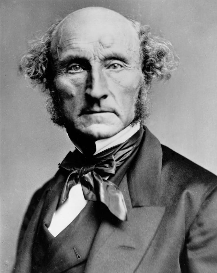 A black-and-white photograph of a bald middle-aged man in late 19th-century dress (John Stuart Mill).k