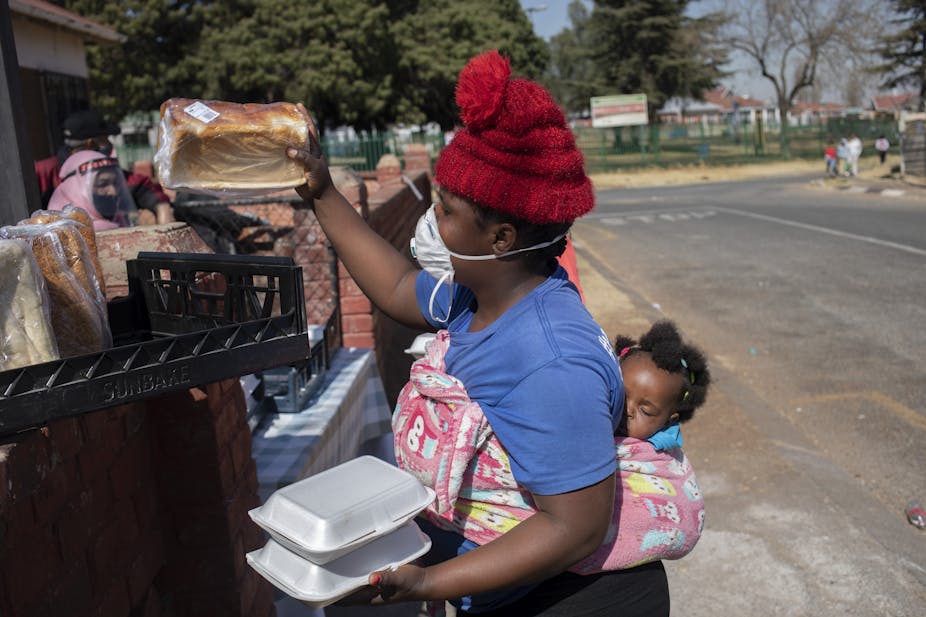 A woman with a baby on her back receives a loaf of bread. 