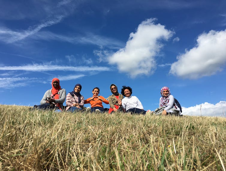 A group of women sit smiling in a field.