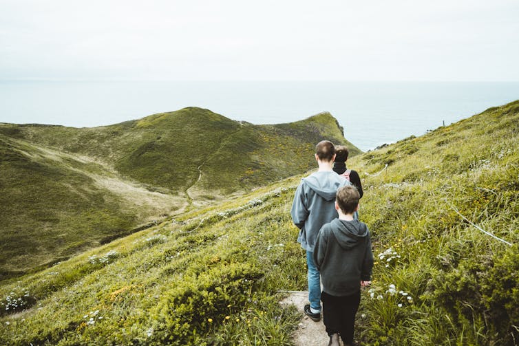 Three people walk through across a cliff towards sea.