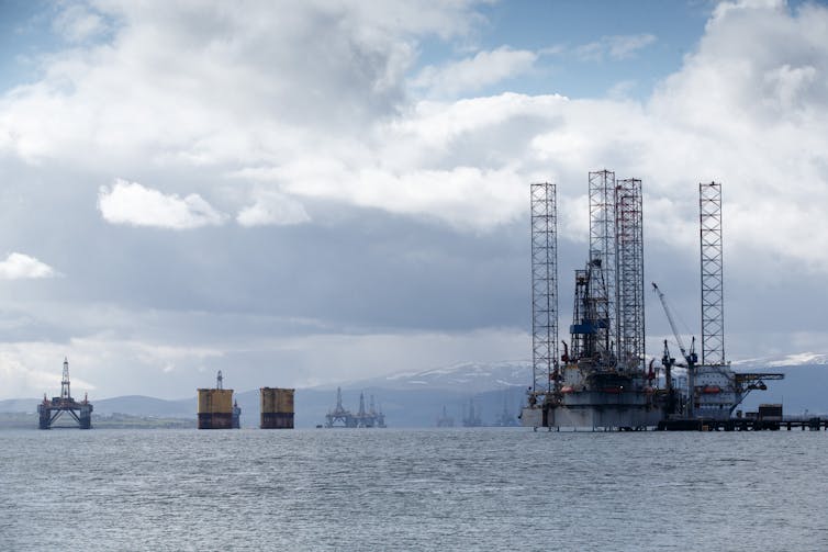Drilling and shallow-water rigs dot the horizon of a large expanse of water.