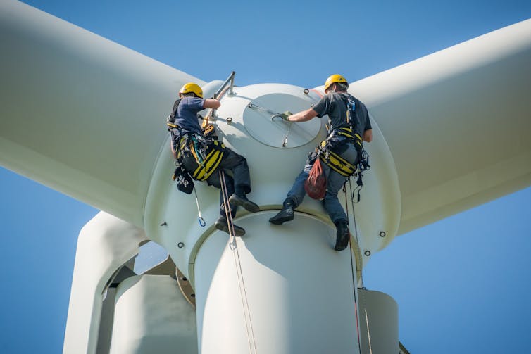 Two engineers in harnesses attend to a wind turbine.