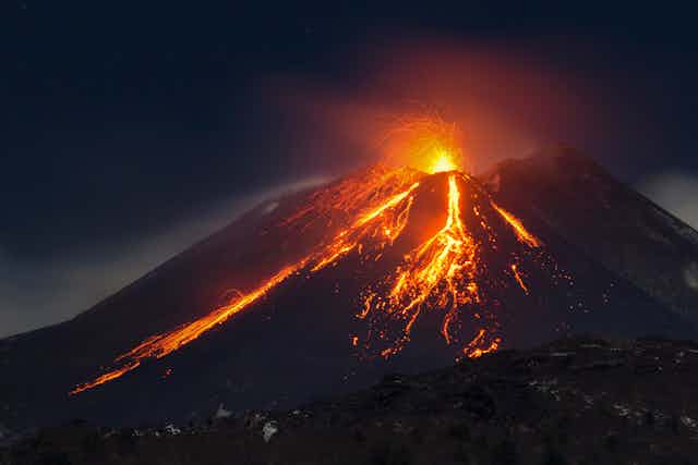 Volcano erupting at night, lava flowing
