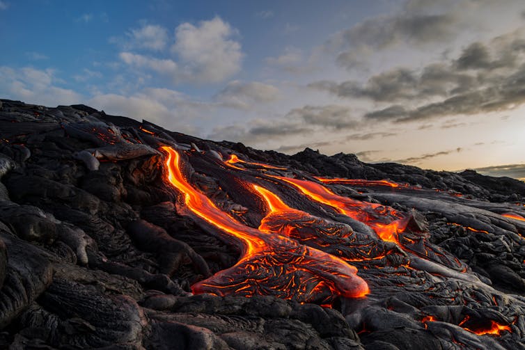 Molten lava flowing down hill of solidified lava