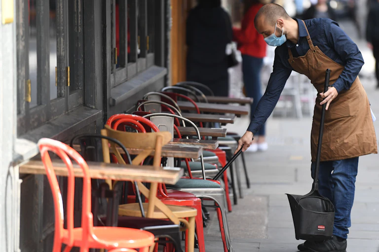 A man wearing a mask cleans tables at a cafe