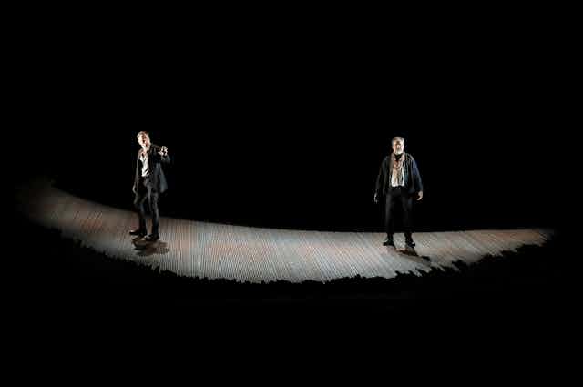 Two men onstage in light with dark surrounds. 