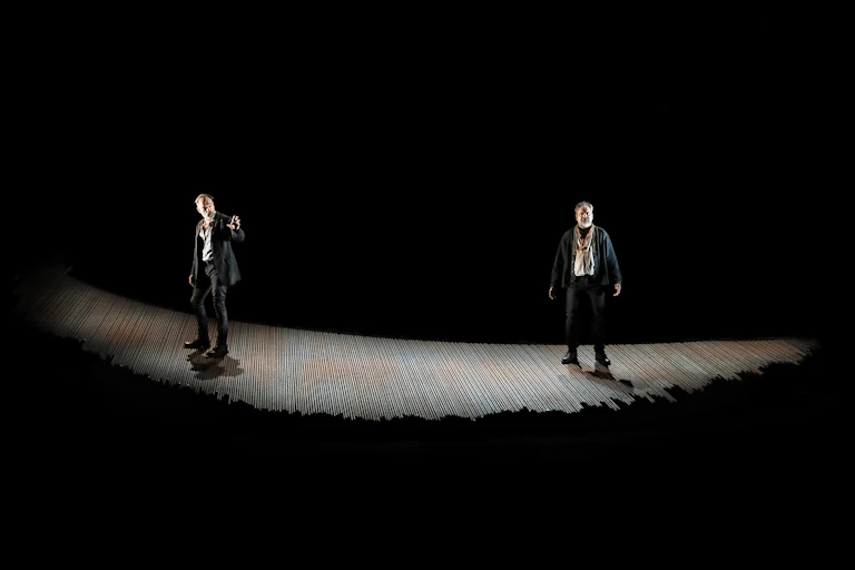 Two men onstage in light with dark surrounds.
