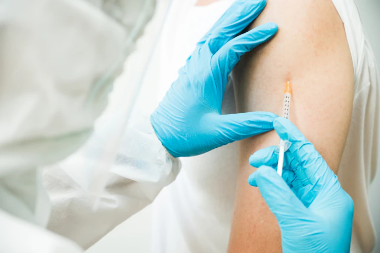 Doctor or nurse in protective clothing injecting an adult in the upper arm