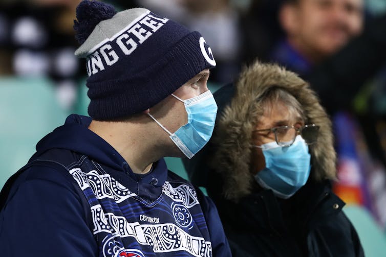 Two people watching a sports match wearing masks