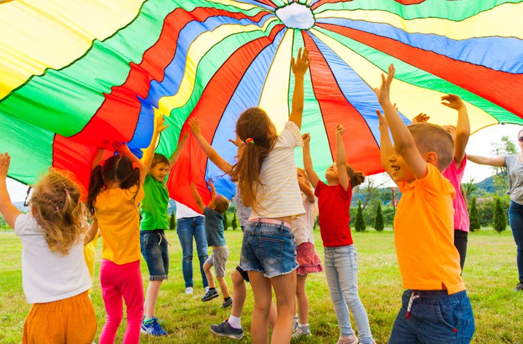 Children playing outside under a colourful parachute