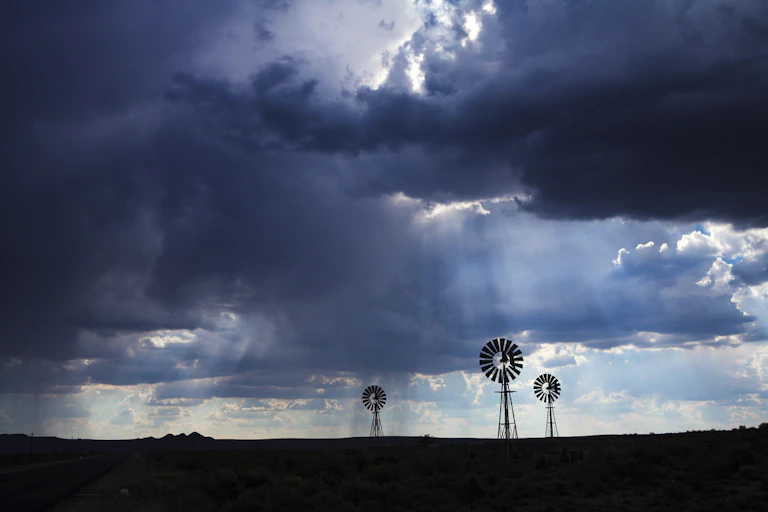 Thick clouds with sun shining through. WIndmills in the foreground.