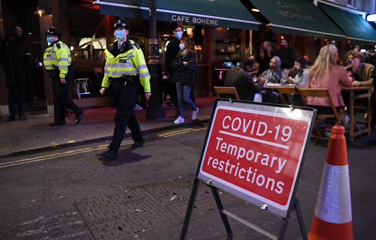 Police in London wearing masks patrol a busy street in Soho.
