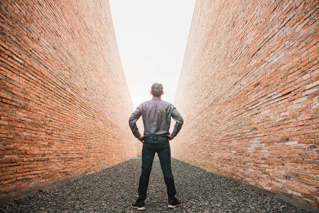Un hombre de espaldas entre dos muros de ladrillo y luz al fondo.