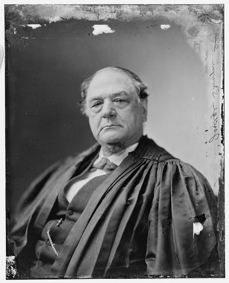 A black and white photograph shows a heavyset white man wearing judicial robes and staring into the camera.