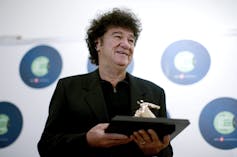 A man with dark curly hair dressed in black holds a trophy.