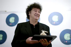 A man with dark curly hair dressed in black holds a trophy.